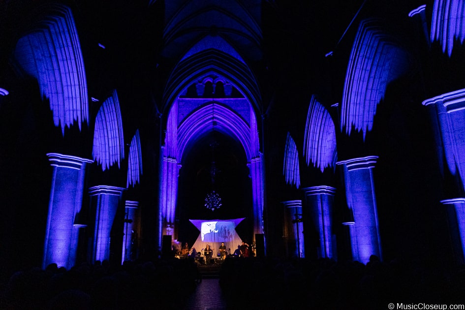 Southwark Cathedral lit up in blue with Seth Lakeman and band playing on stage in the distance