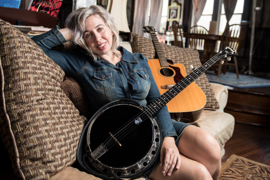 Mean Mary on a sofa holding a black banjo