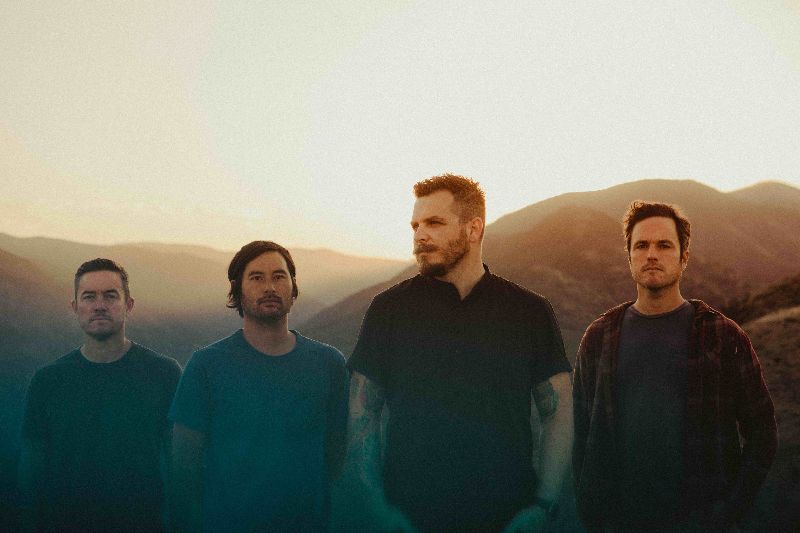 Thrice UK tour 2022 promo photo of the four members of  the band Thrice standing in front of mountains at sunrise