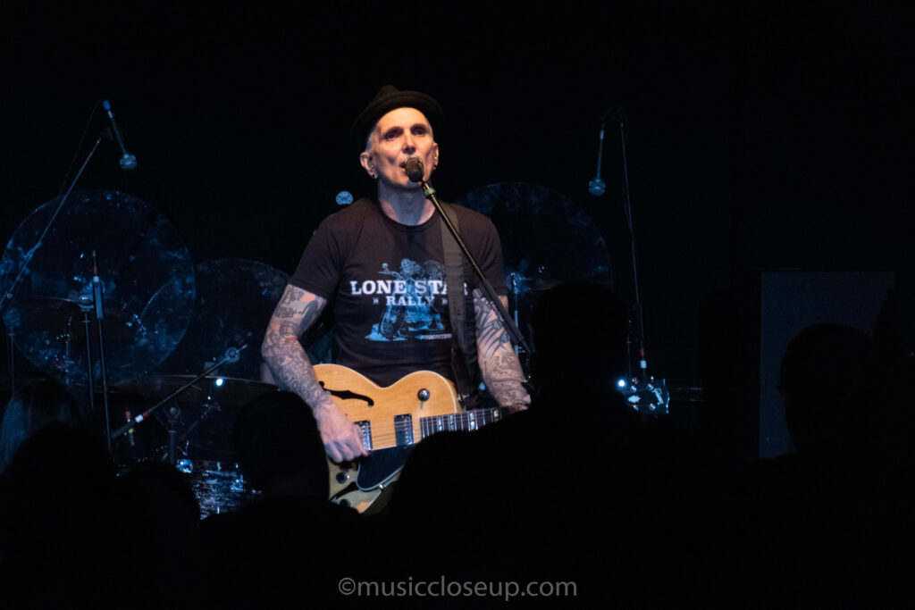 Art Alexakis of Everclear playing guitar. Members of the audience appear as silhouettes in front of him.