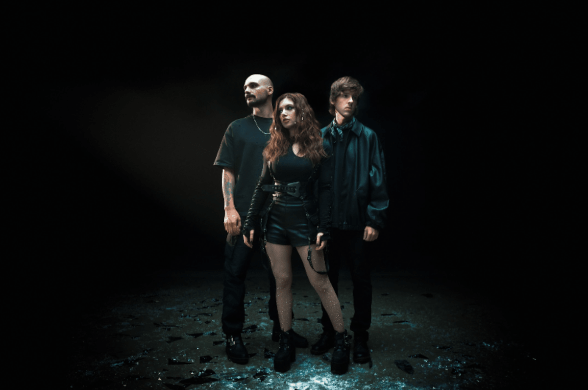 Against The Current tour dates promo photograph of the three band members wearing black in a black room