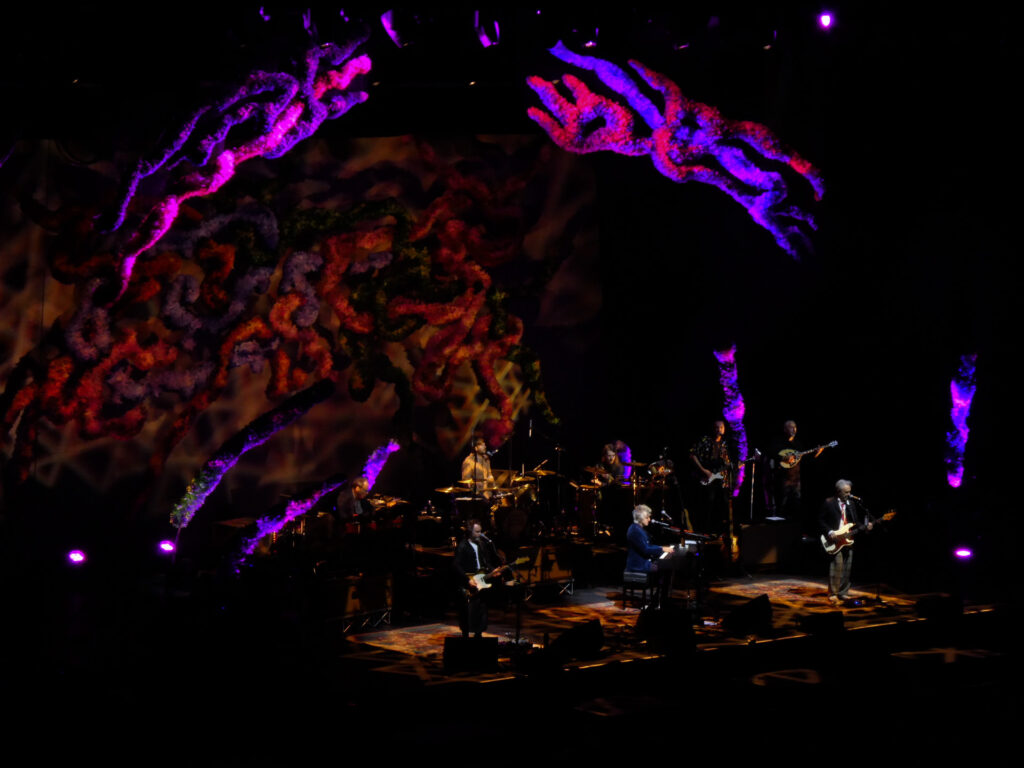 Crowded House at Glasgow Ovo Hydro on October 9, 2024, playing in front of a stage background of fuzzy, colourful swirling shapes