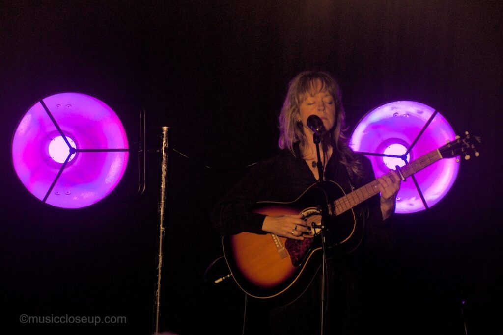 Emily Barker on stage in Dumfries flanked by two big purple lights