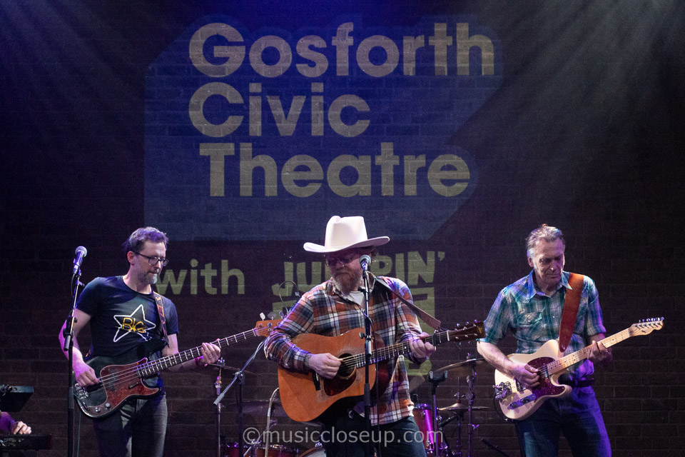 Danny and the Champions of the World live showing Joe Bennett, Danny George Wilson wearing a white cowboy hat, and Paul Lush all playing their instruments.