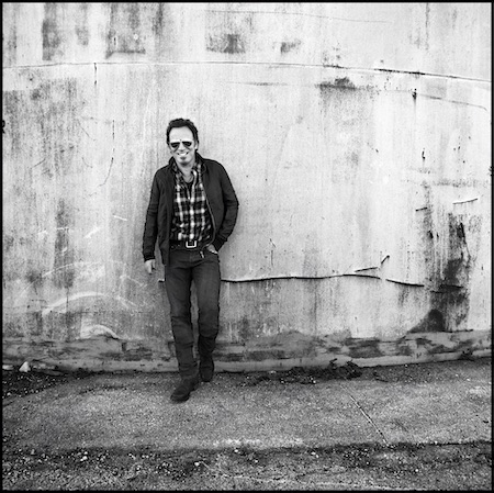 Bruce Springsteen lost albums promo photo: a black & white photo of Springsteen standing against a wall wearing sunglasses