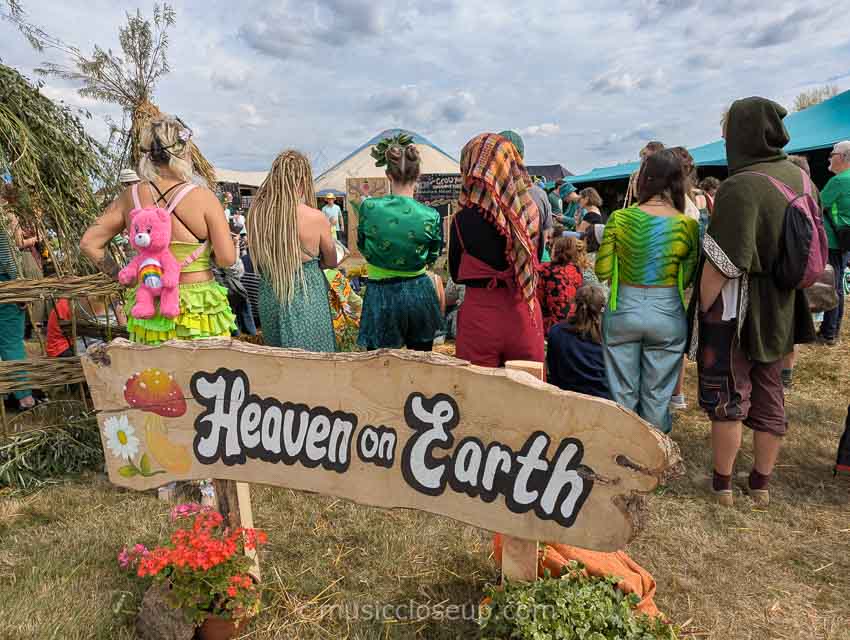 Shambala Festival 2025 review photo: Festival goers standing in front of a sign which reads 'Heaven on Earth'