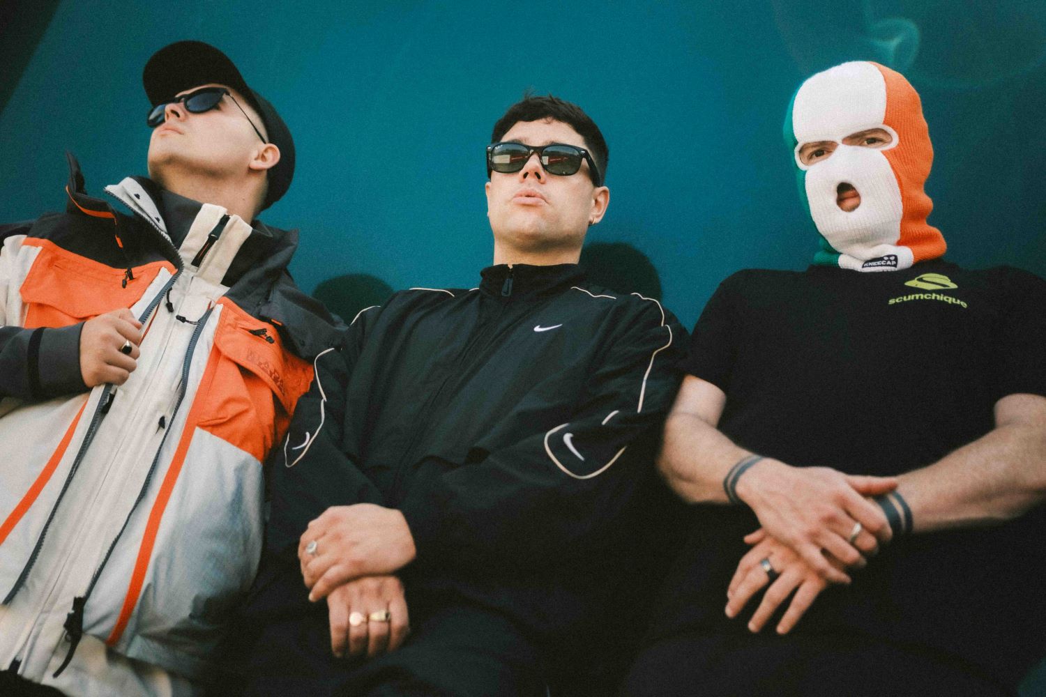 Kneecap Crystal Palace Park - photo of three band members, one wearing a balaclava in the colours of the Irish flag