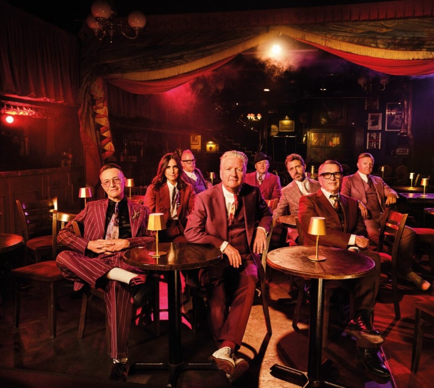 Squeeze and Billy Bragg tour promo - eight members of Squeeze wearing similar suits, sitting in a small speakeasy style venue